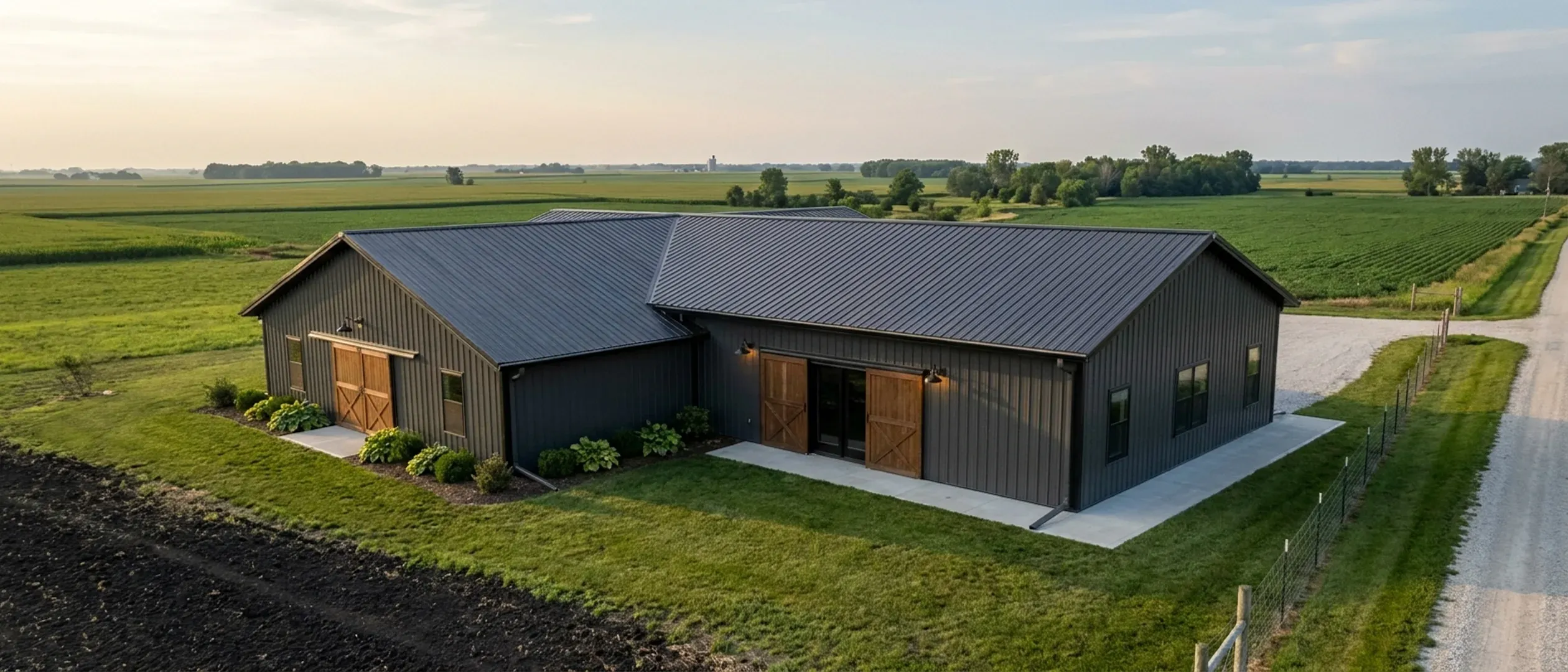 A completed barndominium viewed from a low angle showing its standing seam metal roof, vertical wall panels, gutters and exterior wall lights.